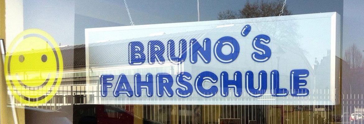 Das Schaufenster von Bruno’s Fahrschule in Witten: der blaue Schriftzug „Bruno’s Fahrschule“ hinter der Scheibe, links daneben ein großer gelber Smiley