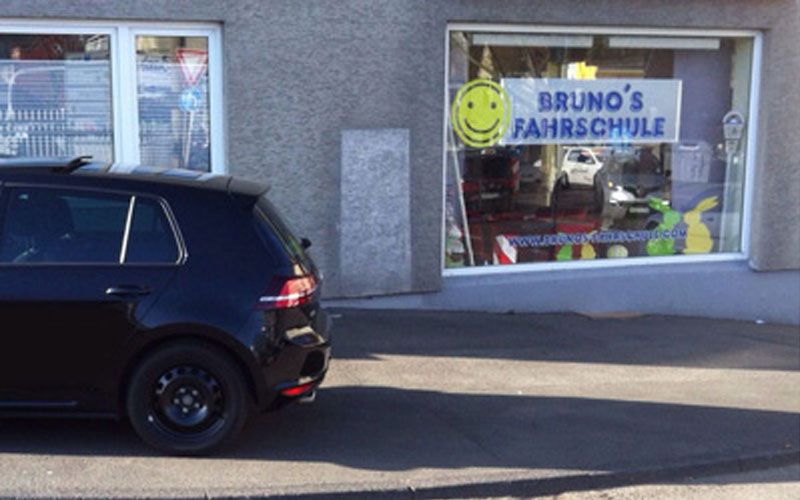 Filiale von Bruno’s Fahrschule in Witten mit gelbem Smiley im Schaufenster und dem Fahrschulwagen davor